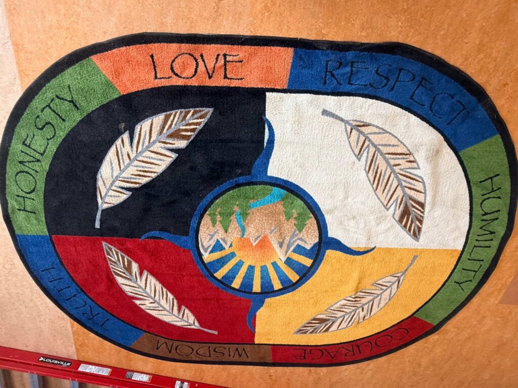 A rug depicting the colours of the medicine wheel and the seven teachings, with some nature graphics.